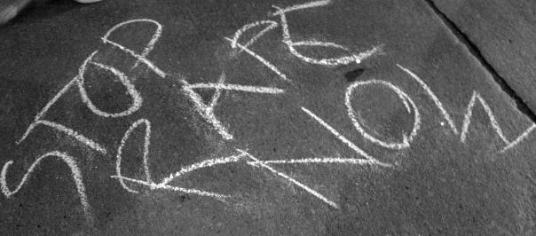 chalk writing on a pavement saying STOP RAPE NOW